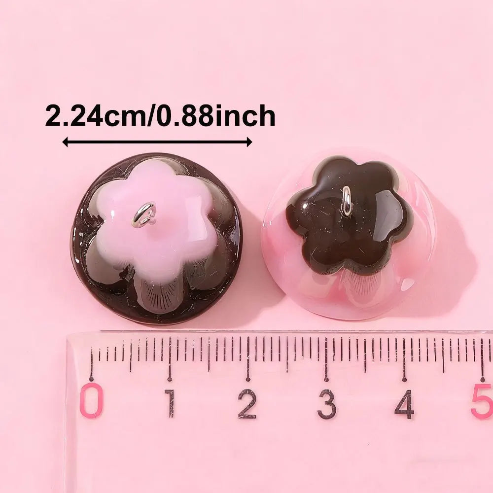 Two pink and black pudding-shaped resin pendants are shown next to a ruler for scale.