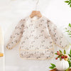 A white waterproof baby bib with long sleeves featuring a delicate floral pattern, hanging on a wooden hanger.
