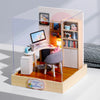 A clear acrylic display box featuring a wooden miniature dollhouse kit with shelves and furniture.