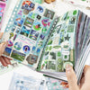 Eine Hand hält ein offenes Stickerbuch mit Natur- und abstrakten Aufklebern zum Scrapbooking