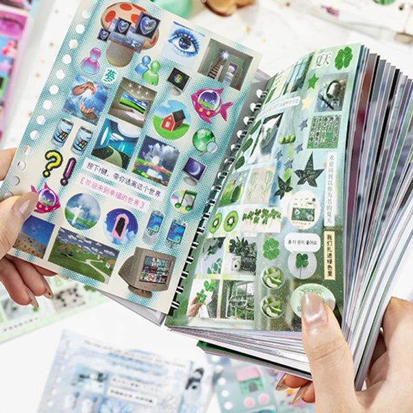 A hand holds an open art paper sticker book filled with various nature and abstract themed stickers for scrapbooking