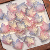Pink and blue maple leaf glass beads scattered on a light background for DIY jewelry making
