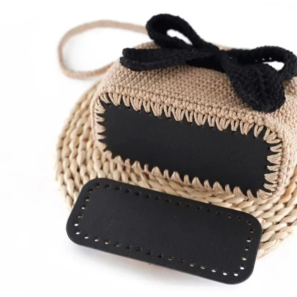 A beige crochet bag with a black rectangular bottom featuring pre-punched holes and a black bow.