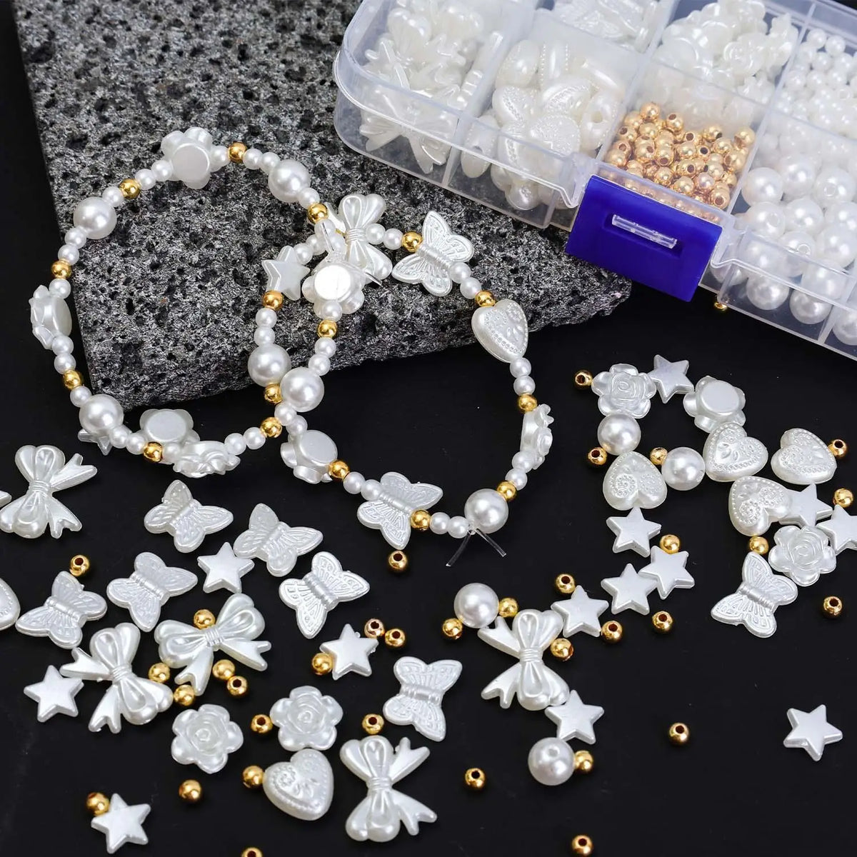A collection of white and gold pearl beads, including various shapes like flowers, stars, and hearts, displayed with plastic 