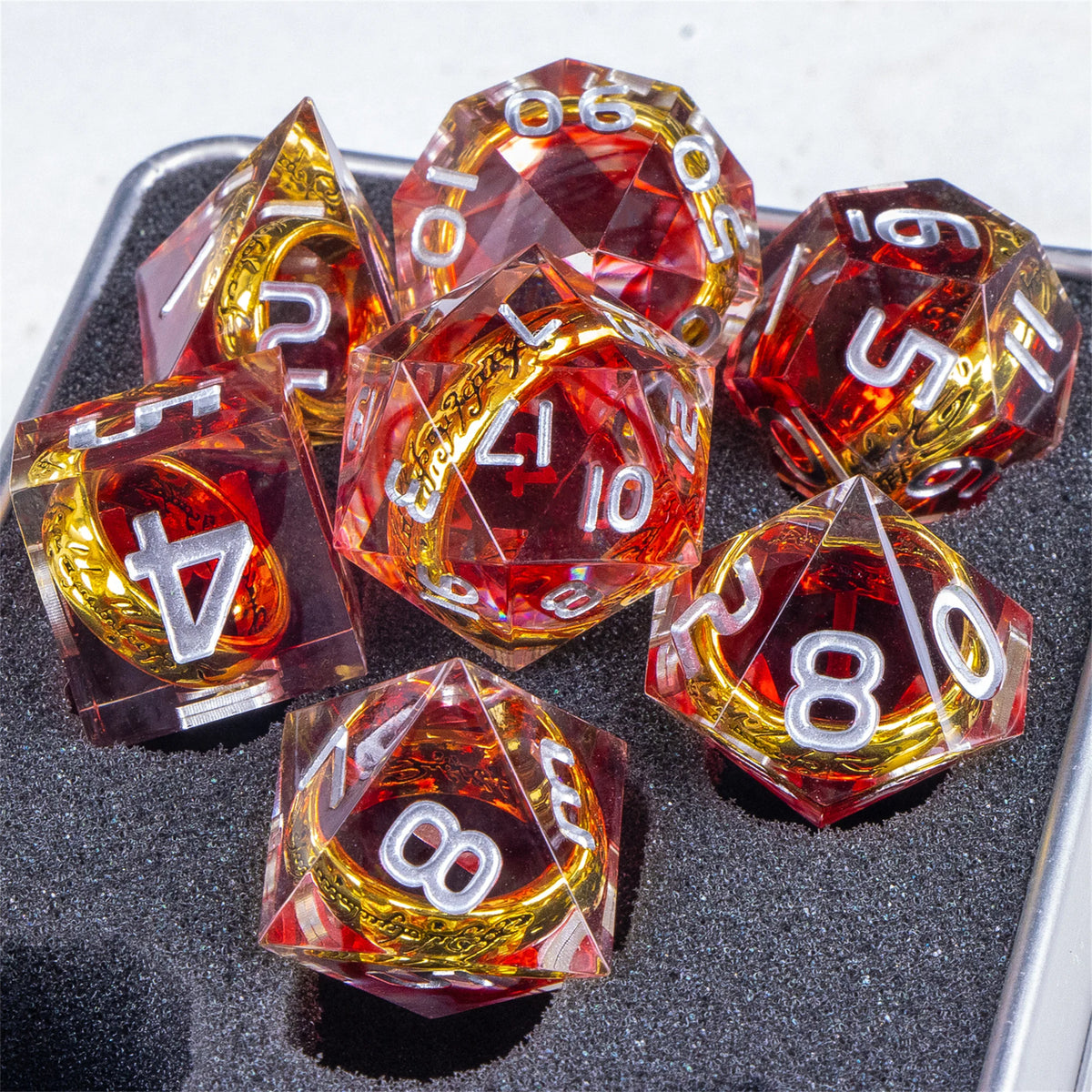 A collection of translucent red resin dice with golden elven numbers scattered on a dark surface.