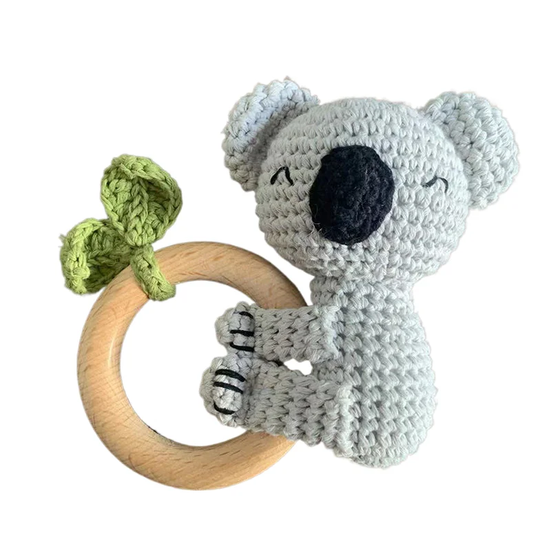 A gray crocheted otter toy with a black nose sitting on a natural wood ring.