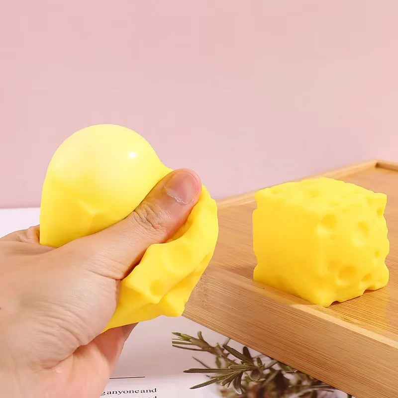 A hand squeezes a bright yellow, squishy cheese-shaped fidget toy on a wooden surface.