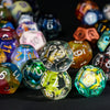 A close-up shot of a collection of colorful polyhedral resin dice scattered on a dark surface.