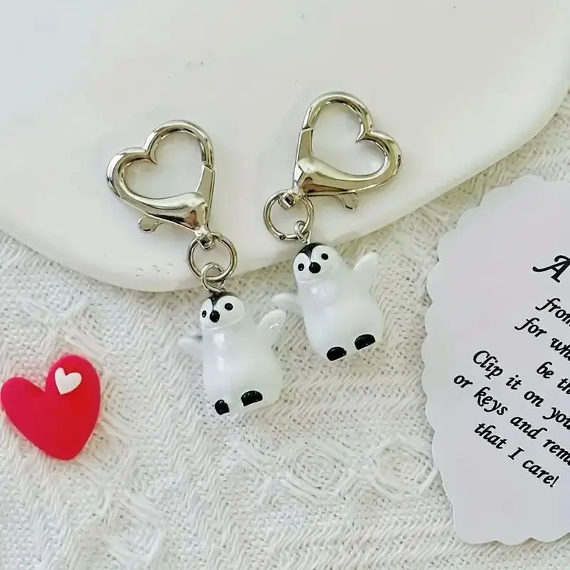 A set of silver heart-shaped keychains featuring white and black penguin figures.