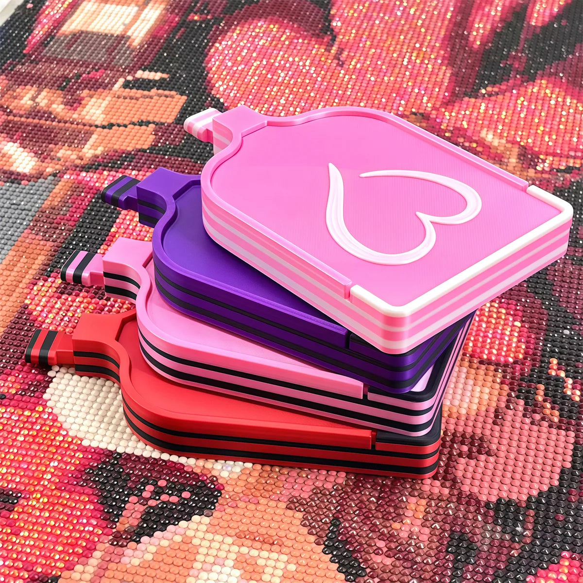 A stack of pink and purple diamond painting storage trays and organizer boxes on a sparkly background.