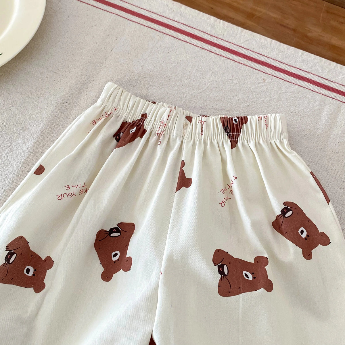 White casual pants for kids with a plaid print pattern and elastic waist visible on a light fabric background.