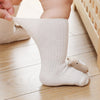 A close-up of a beige cotton sock for a baby or toddler, featuring a small stitched animal detail.
