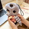 A hand holds a plush dinosaur skeleton bag charm with a removable hood and a small accessory on a white table.