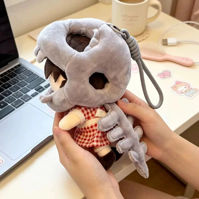 A hand holds a plush dinosaur skeleton bag charm with a removable hood and a small accessory on a white table.