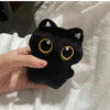 A hand holds a black plush cat with large yellow eyes against a white background.