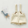 A pair of beige toddler denim romper with chest pockets lying next to a card that reads Faith Hope Love.