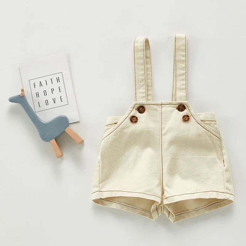 A pair of beige toddler denim romper with chest pockets lying next to a card that reads Faith Hope Love.