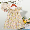 A yellow floral smocked summer dress for girls with pink accents, displayed on a hanger against a light background.