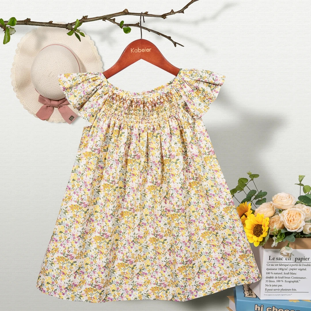 A yellow floral smocked summer dress for girls with pink accents, displayed on a hanger against a light background.