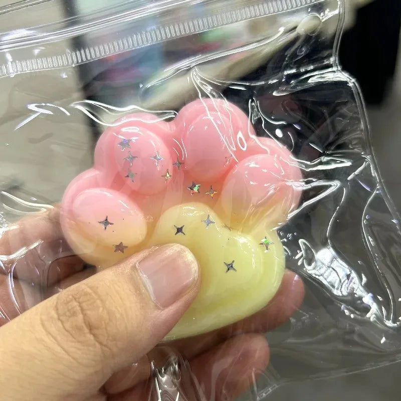 A hand holds a pink squishy product with yellow accents and glitter inside clear plastic packaging.