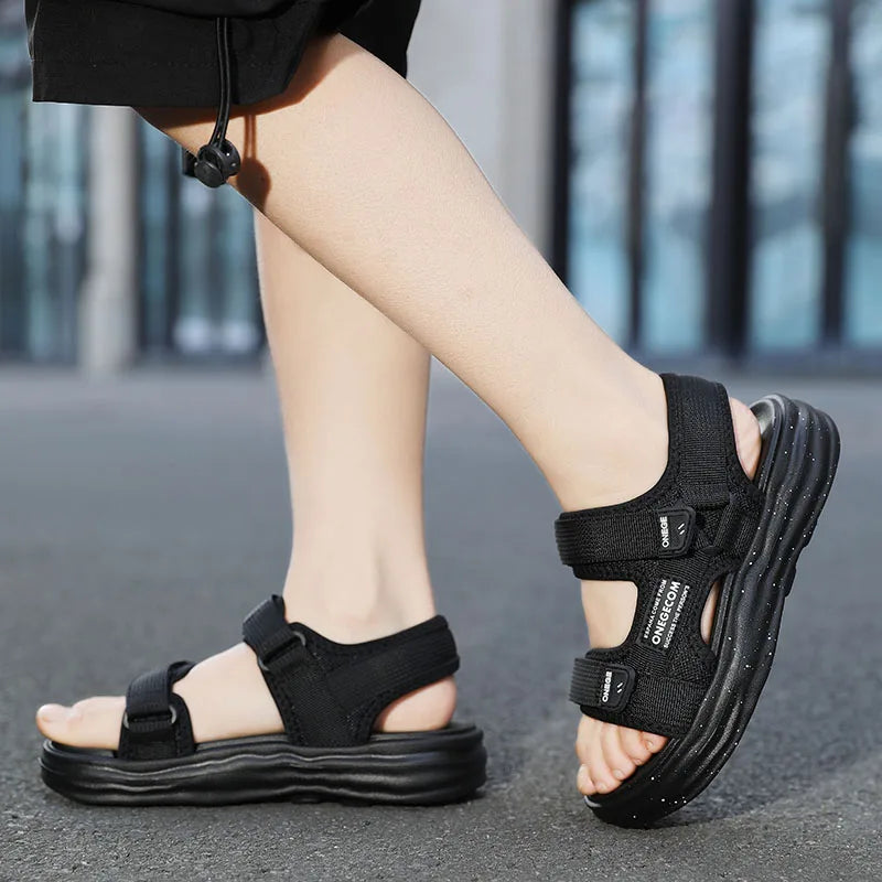 A close-up shot of a pair of black boys' non-slip summer sport sandals worn on a person's foot.