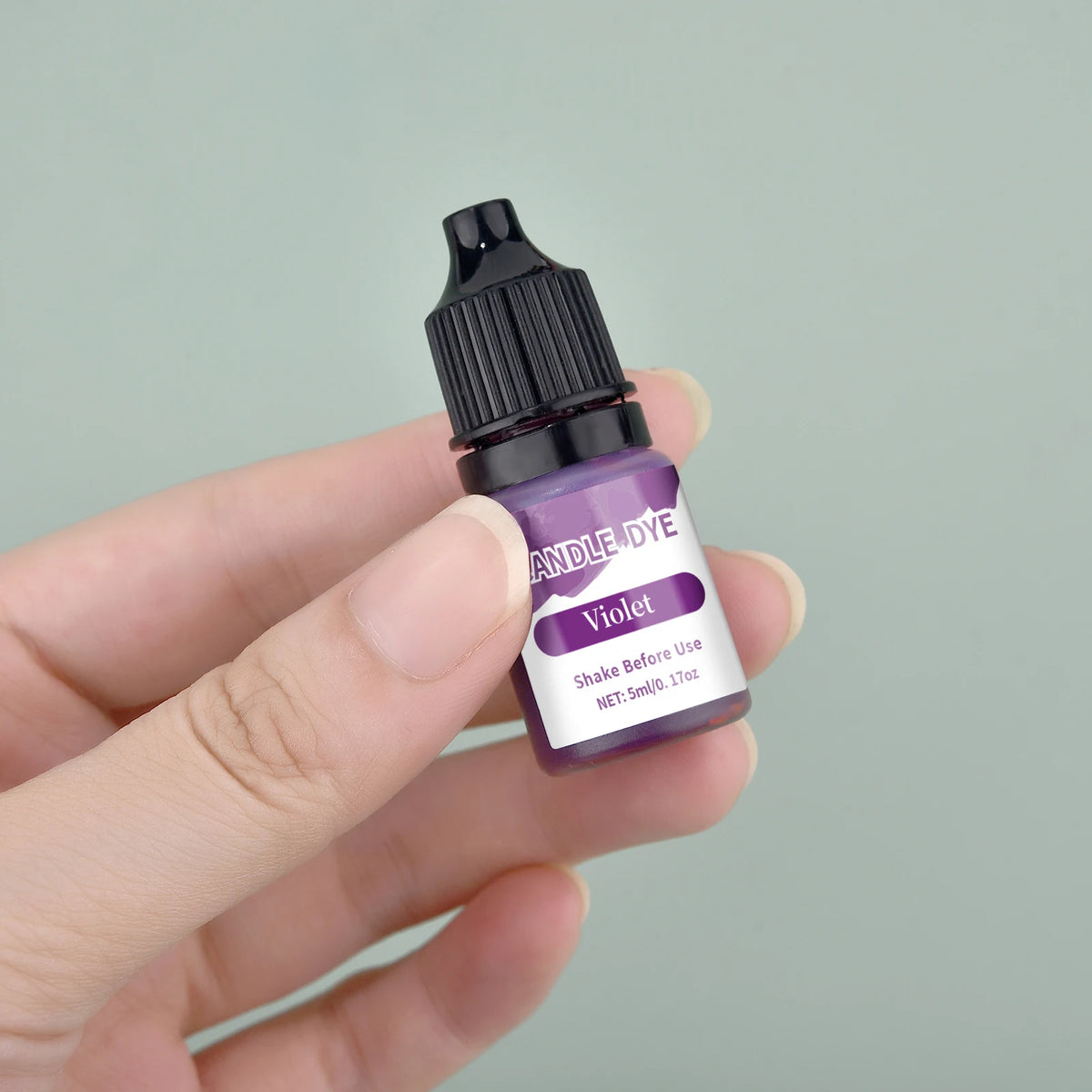 A hand holds a small dark bottle of violet liquid candle dye labeled Violet for DIY wax projects.