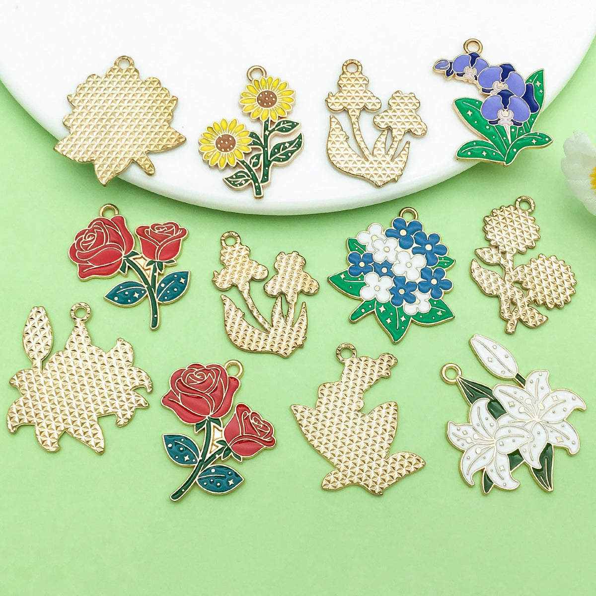 A collection of enamel flower charms in various colors including gold, yellow, blue, red, and white on a light green backgrou