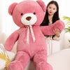 A large pink teddy bear plush toy sitting on a white sofa next to a young woman.