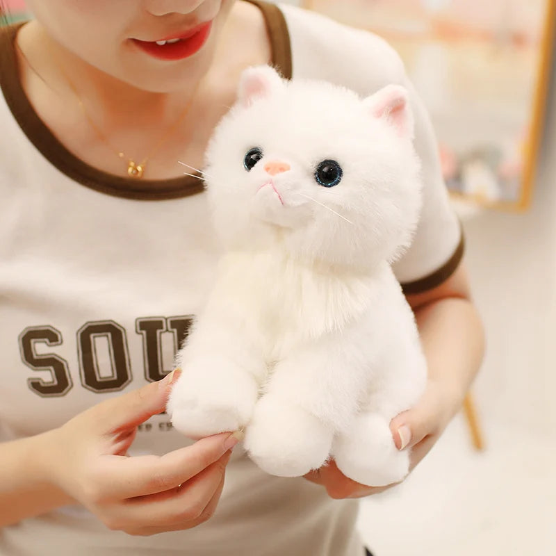 A person is holding a white fluffy kitten plush toy against their chest.