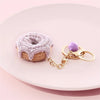 A handmade crochet fruit keychain pendant shaped like a donut resting on a pink plate.