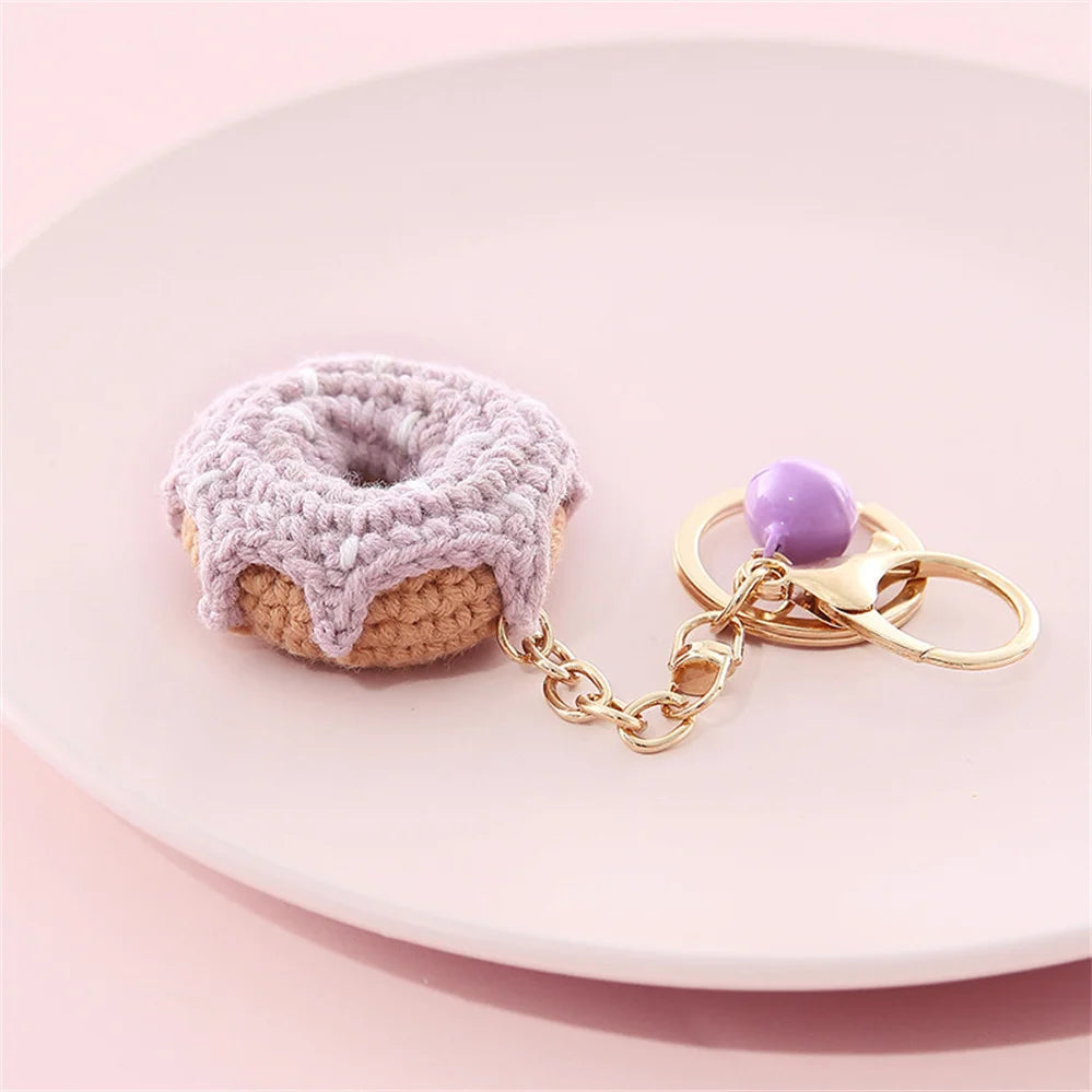 A handmade crochet fruit keychain pendant shaped like a donut resting on a pink plate.