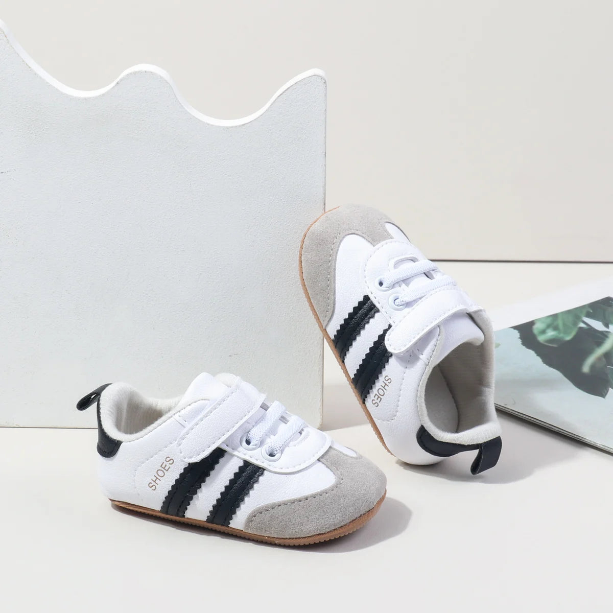 A pair of white baby first walkers shoes with black and gray stripes resting on a white background.