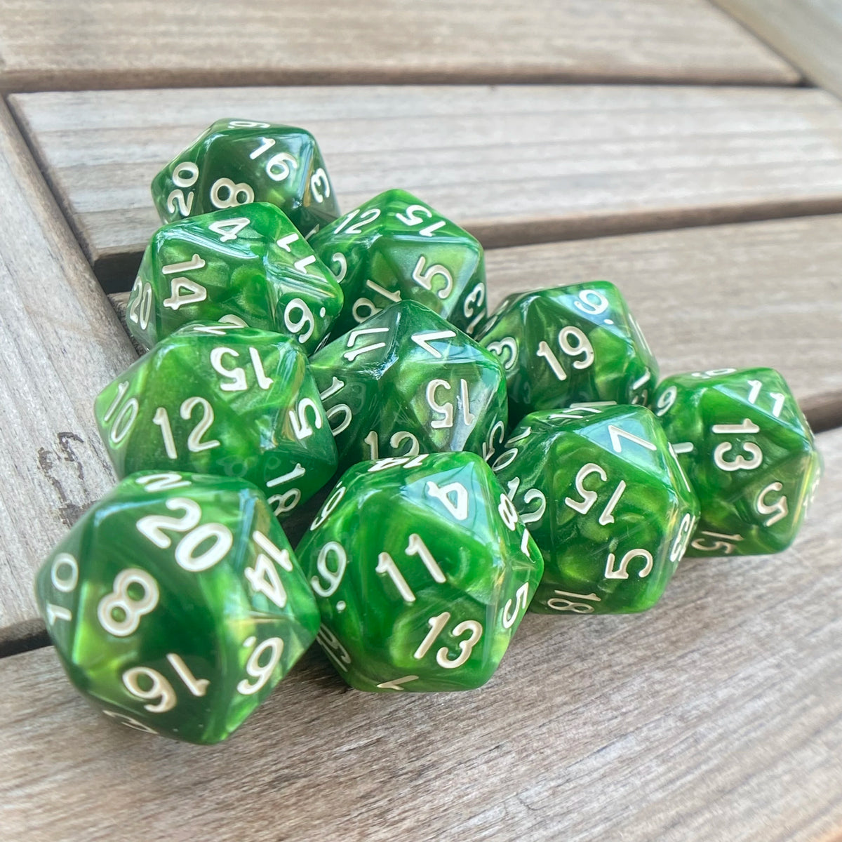A collection of ten green pearl acrylic D20 dice scattered on a wooden surface.