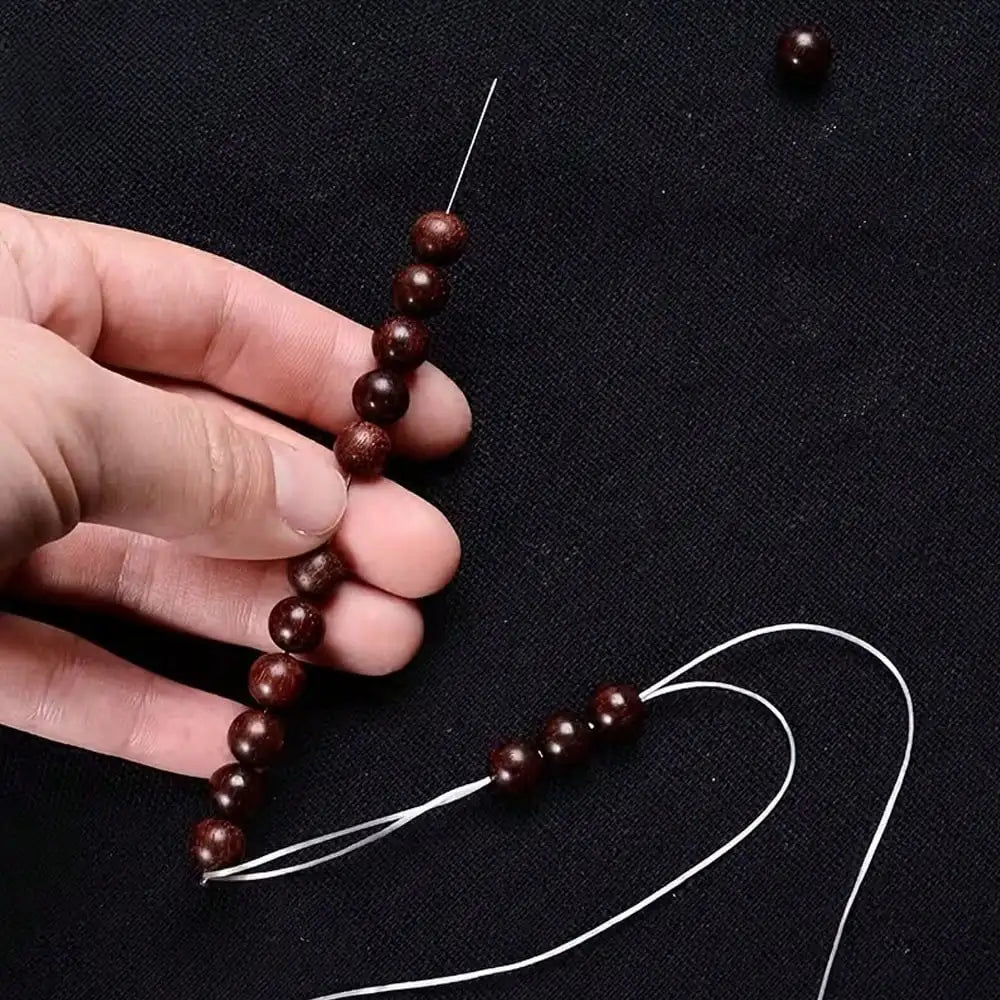A hand holds a string of dark brown metal beads threaded onto a needle, with loose threads extending from the beads.