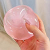 A hand holds a translucent pink mochi squishy stress relief toy against a light background.