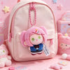 A pink backpack featuring a small plush charm of a character with pink hair and a blue outfit.