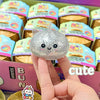 A hand holds a silver glitter unicorn bun squishy toy with cute facial features against a colorful packaging background.