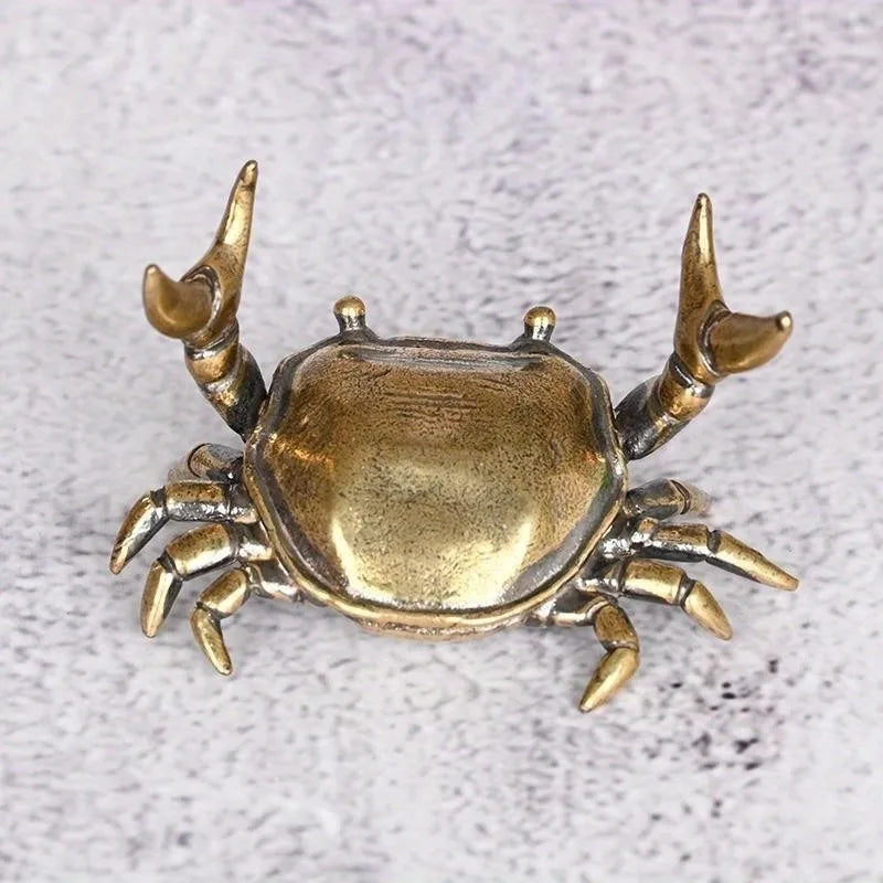 A brass crab figurine statue with detailed claws and body, displayed against a light gray background.