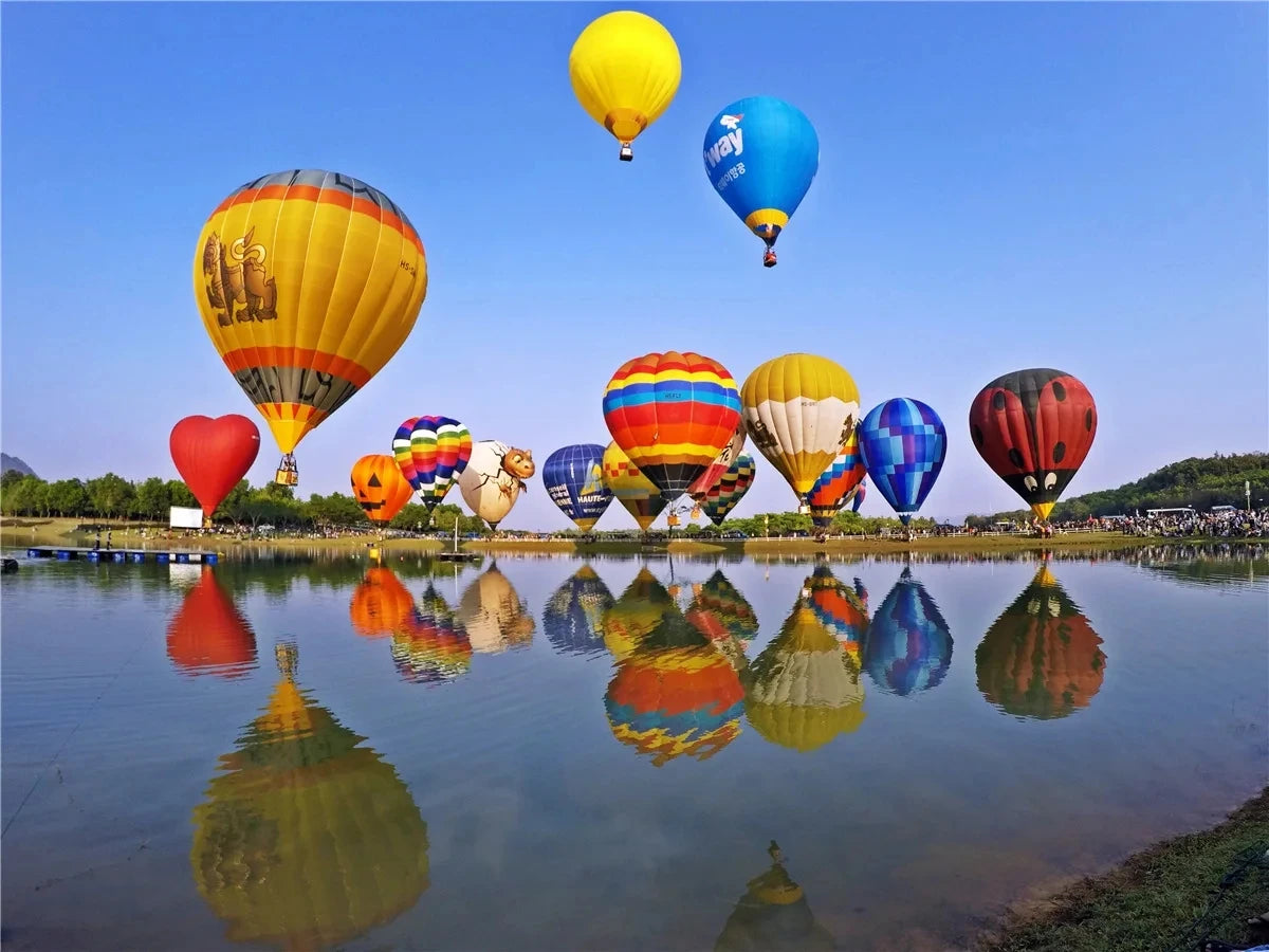 A collection of colorful hot air balloons floating above water, reflected in the calm surface.