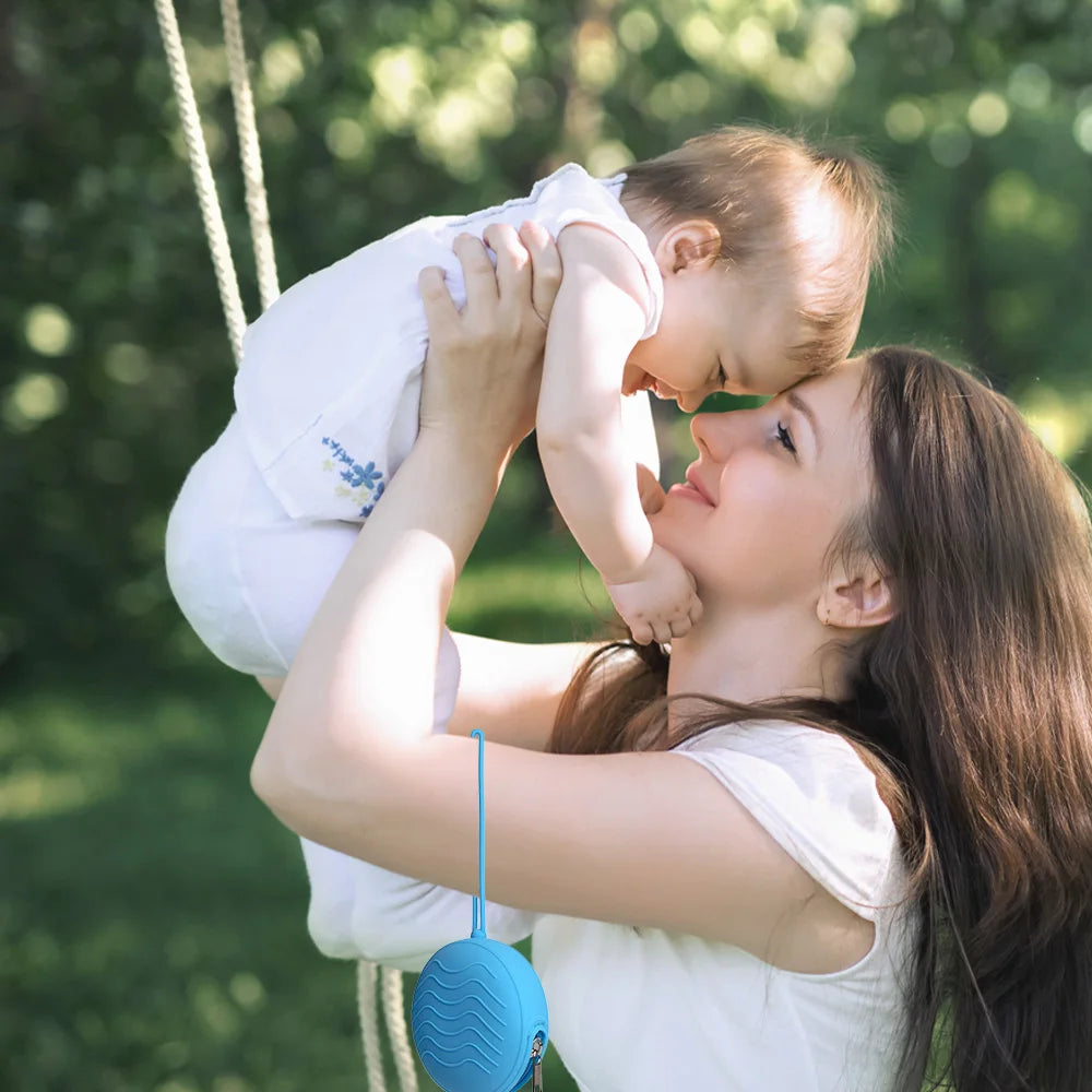 A woman is holding a baby in a silicone pacifier holder outdoors.