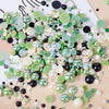 A scatter of mixed resin rhinestone pearls in various shades of green, white, and black.
