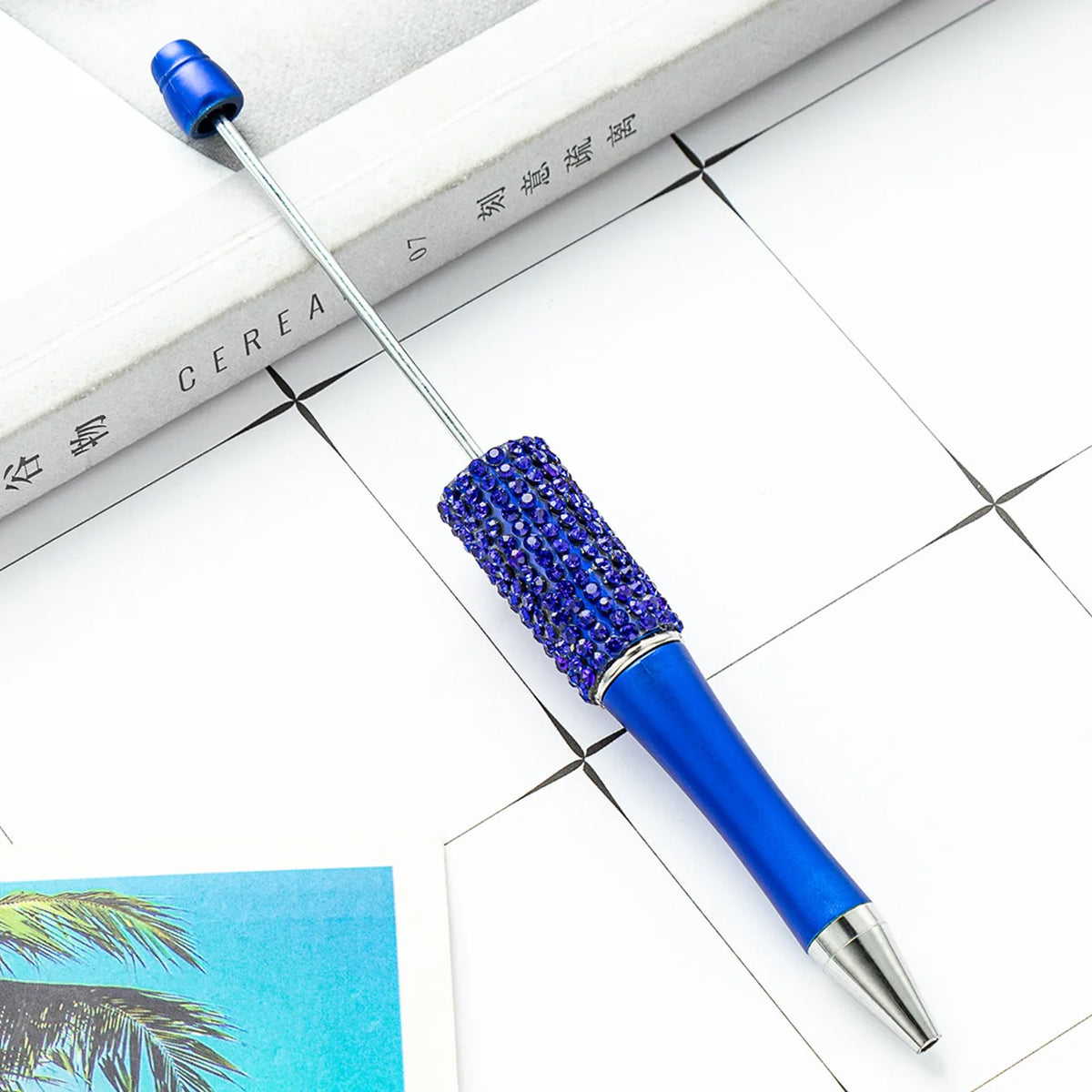 A blue and silver beaded ballpoint pen craft kit with a metal tip resting on a white surface.