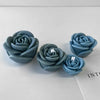 Three silicone molds shaped like roses in a muted blue-green color resting on a white surface.