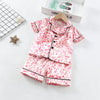 A pink leopard print toddler pajama set with a collar and buttons is displayed on a white surface.