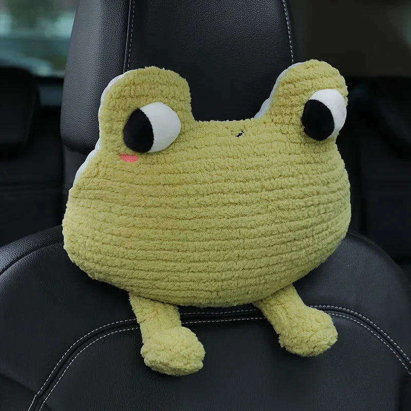 A light green plush toy resembling a frog with large eyes sitting on a black car seat.