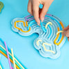 A hand is placing colorful silicone tubes into the grooves of a blue cloud-shaped sensory busy board.