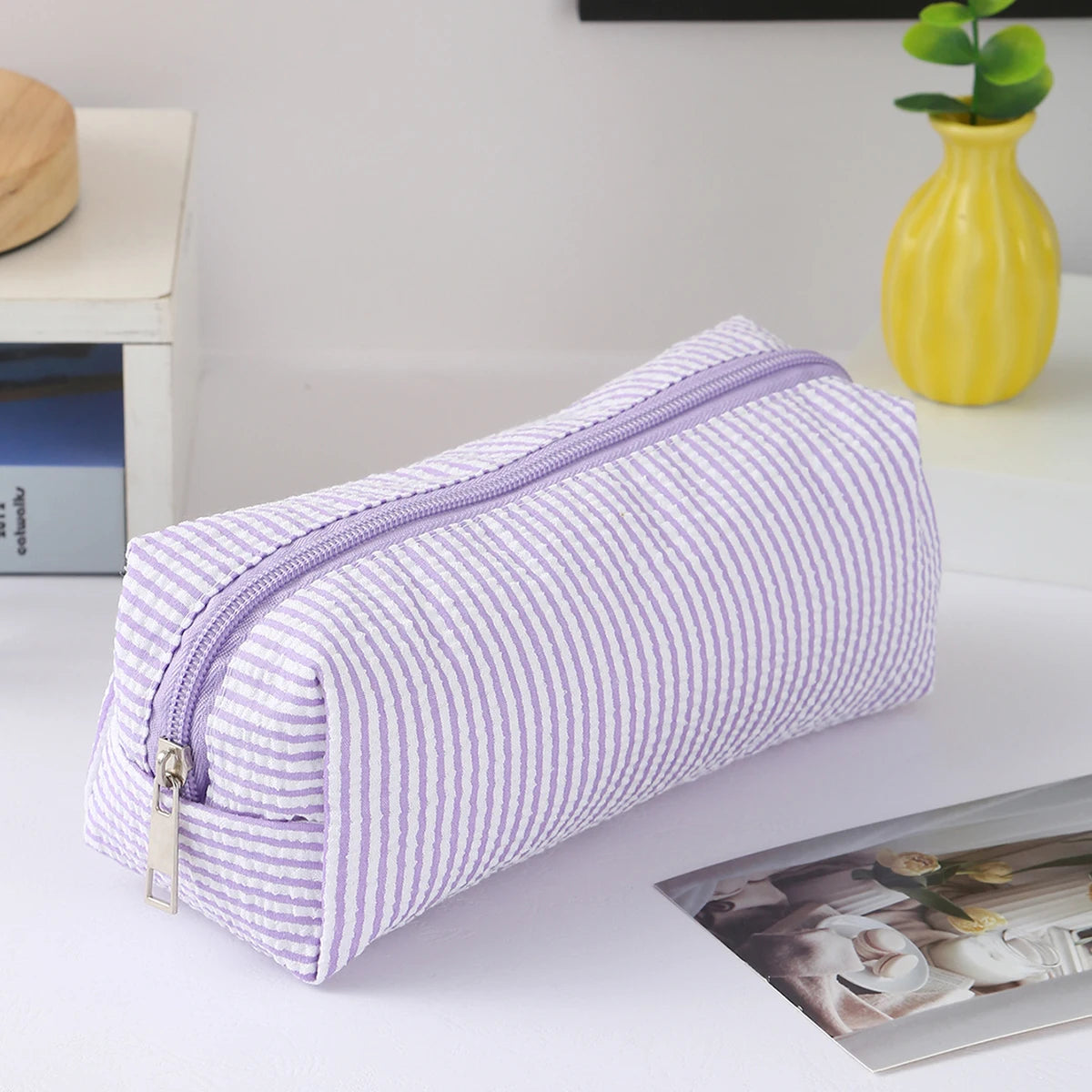 A purple and white striped canvas pencil case with a zipper is displayed on a white surface.