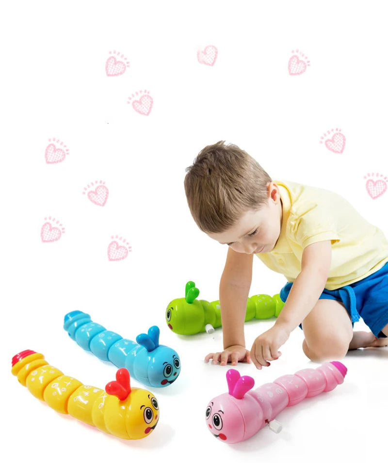 A young boy is interacting with several colorful wind-up caterpillar crawling toys.