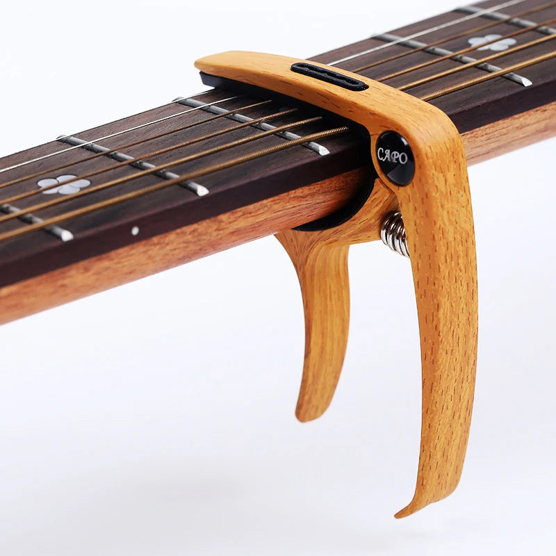 A wooden guitar capo with a metal pick holder is shown on a fretboard.