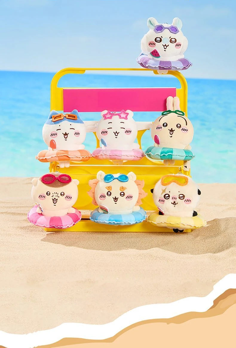 A yellow plastic container holds several cute Chiikawa summer swimming ring plush keychains on a sandy beach.